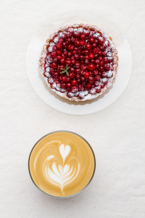Coffee with milk (cappuccino or flat white) and lingonberry tart on a light cloth background. Breakfast in a coffee shop.Top viewの写真素材