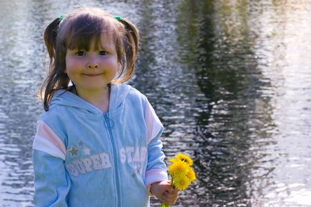 Little girl with dandelions bouquet smilimg over open water backgroundの写真素材