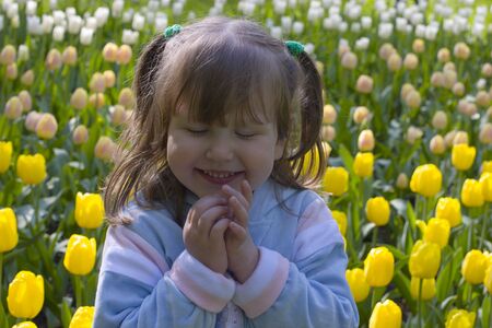 Happy excited smiling little girl over different colored tulips backgroundの写真素材