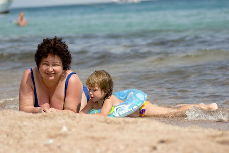 Grandmother and grandchild lying in the water on the beach hot sunny dayの写真素材