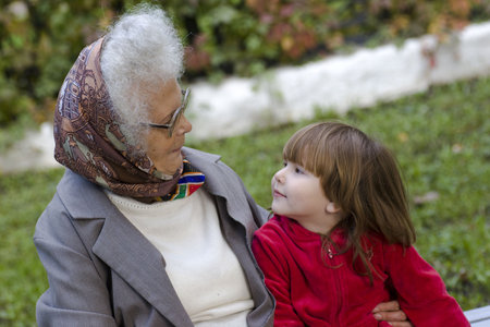 Great grandmother talking to her little grandchild on the bench in the park