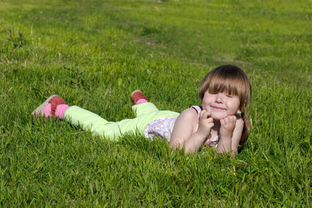 Happy smiling girl resting on vivid fresh green grass under the sun, her eyes closed, の写真素材