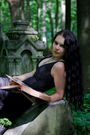 Gothic girl with old book posing on gravestoneの写真素材