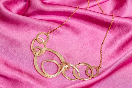 Beautiful shiny golden asymmetric necklace with different circle forms over pink backgroundの写真素材
