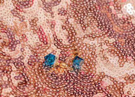 Pair of modern golden earrings with blue gemstones on golden shiny backgroundの写真素材
