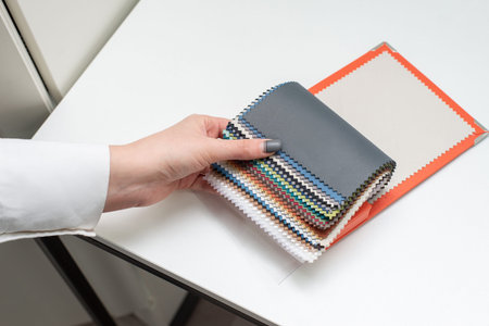 multicolored textile samples catalog for selection female hand white table