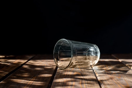 Empty transparent glass on a dark horizontal background. brown wooden table. bright sun