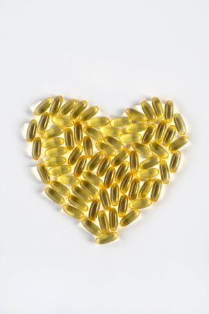 handful of yellow heart-shaped pills on a white background vitamins care health oil fish oilの写真素材