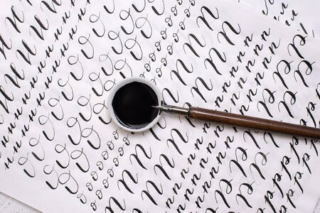 Calligraphy sheets, nibs, paper, ink on a wooden background. Lettering calligraphy workshop. Letters of the English alphabet written with a paint brush. Concept hobby. close-up, top view, flat lay.の写真素材