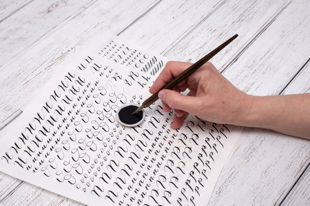 Calligraphy sheets, nibs, paper, ink on a wooden background. Letters of the English alphabet written...