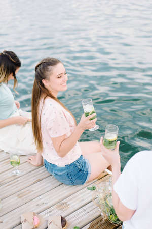 beautiful girls sitting on a wooden pier near lake. rest, picnic,lemonadeの写真素材