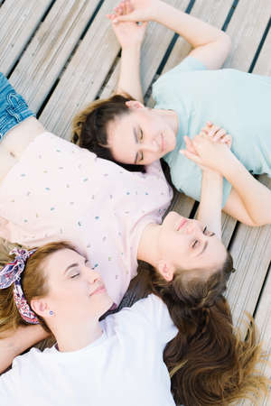 three girls lie with closed eyes on a wooden pier. rest, picnicの写真素材