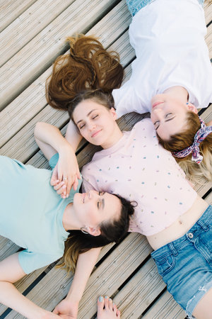 three girls lie with closed eyes on a wooden pier. rest, picnic