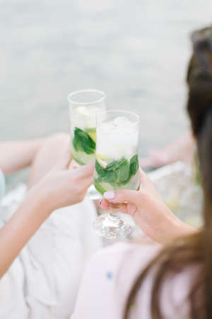Girls holding fresh lemonade in glass. Healthy vegan lifestyle. Eco-friendly in the nature. Lemons, oranges with mint in the glassの写真素材