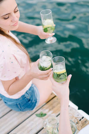 Girls holding fresh lemonade in glass. Healthy vegan lifestyle. Lemons, oranges with mint in the glass.の写真素材