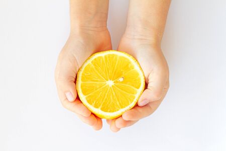 Childrens hands holding a lemon close up on a white backgroundの写真素材