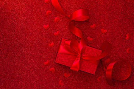 A gift box with a red bow on a red background with hearts. The concept of the day of St....