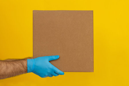 Delivery man holding cardboard boxes on yellow background. Delivery by courier in medical rubber...