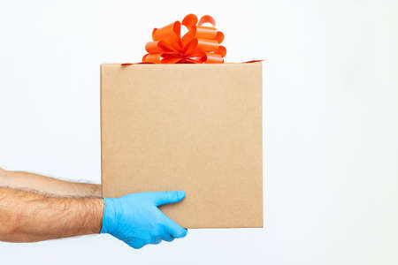 A man in medical gloves holds a box with a red ribbon and a bow on a white background. Sale. Gift. Coronavirus, quarantine, saleの写真素材