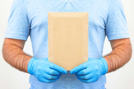 Mens hands in medical gloves hold an envelope with documents. Delivery service. Post service. Mockup.の写真素材