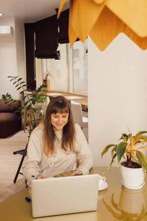 Woman home office and distance remote working. A young female businesswoman sitting at a desk typing on her laptop in a home office,の写真素材