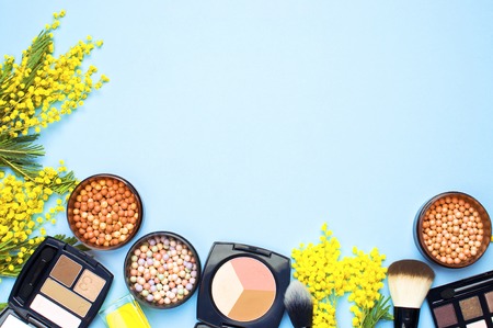 Set of decorative cosmetics for make-up Powder  Eyeshadow Corrector Brushes and flowers of mimosa on blue background. Makeup Accessories Top viewの写真素材