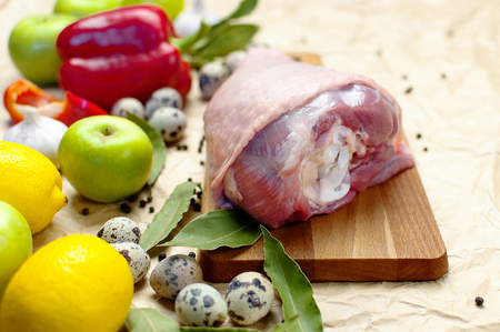 Raw turkey thigh garlic apples lemon red bell pepper quail eggs spices on a wooden board. Top view of a turkey, knife on a beige paper background. Culinary backgroundの写真素材