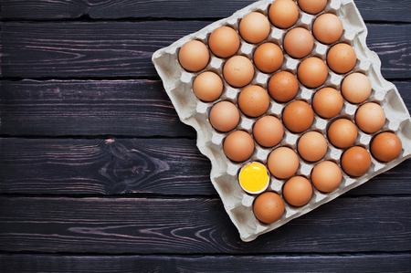 Top view of chicken eggs in a cardboard box on a dark wooden table with copy space. Food background, egg, yolk, dark wooden background.の写真素材
