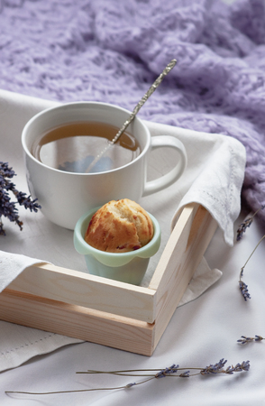 A tray with a cup of hot tea and cupcakes in bed with a knitted blanket. Herbal tea Hot drink Mood Love Message Breakfast in bed Morning Lifestyleの写真素材