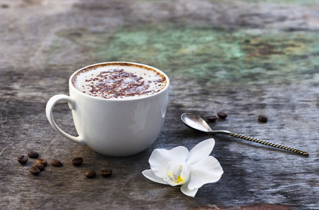 A cup of hot coffee and orchid flower on the wooden background. Traditional drink cappuccino or cocoa Wooden background Orchid flower Autumn drinkの写真素材