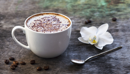 A cup of hot coffee and orchid flower on the wooden background. Traditional drink cappuccino or cocoa Wooden background Orchid flower Autumn drinkの写真素材