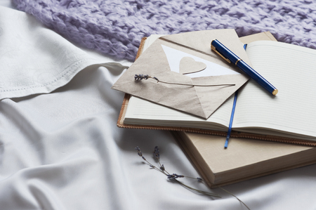 Notepad letter and book with plaid and lavender on white textile in bed. Diary Envelope Lifestyle Plaid Scarf Lavender Cozy backgroundの写真素材
