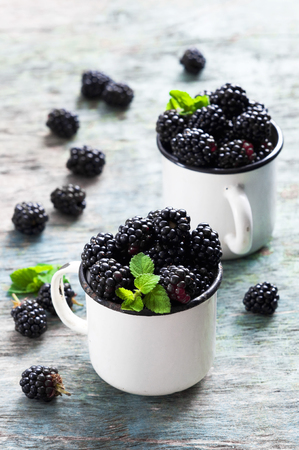 Fresh blackberries with mint leaves in a white cup on a rustic wooden background with copy space. Berry, vitamins, food backgroundの写真素材