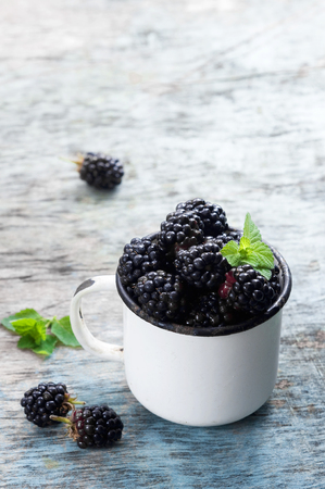 Fresh blackberries with mint leaves in a white cup on a rustic wooden background with copy space. Berry, vitamins, food backgroundの写真素材