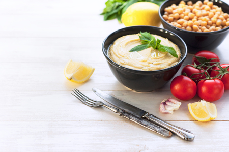 Bowl with hummus, chickpeas, lemon, cherry tomatoes and herbs on a white rustic wooden background. Middle Eastern cuisine. Background hummusの写真素材