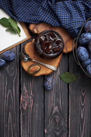 Homemade plum jam in a glass jar and fresh blue plums in a bowl on a dark rustic wooden background with copy space top view. Fruits, vitamins, food backgroundの写真素材