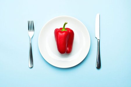 Red bell pepper on a white plate, fork and knife, dieting, healthy food concept. Fresh pepper,...