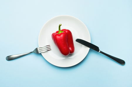 Red bell pepper on a white plate, fork and knife, dieting, healthy food concept.の写真素材