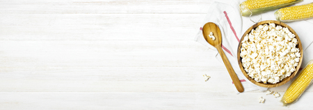 Brown wooden bowl with delicious traditional popcorn, fresh corn and a spoon on a light wooden background. Top view of a light meal background. Corn Dishesの写真素材
