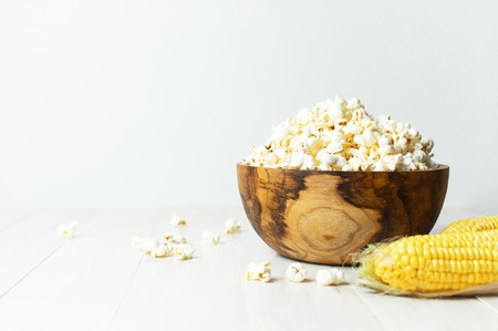 Brown wooden bowl with delicious traditional popcorn on a light wooden background. Top view of a light meal background. Corn Dishesの写真素材