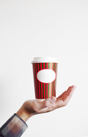 Hand of a man in a plaid shirt with a paper cup of coffee or tea on a white background. Layout for designの写真素材