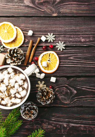A cup of hot coffee with marshmallow, spruce branches, cones, Christmas gifts, mugs of orange, snowflakes, cinnamon, New Year Christmas composition. Traditional festive decoration Christmas dark background top view.の写真素材