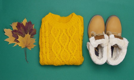 Female orange knitted sweater, boots and autumn leaves on dark green background top view flat lay. Fashion Lady Clothes Set Trendy Cozy Knit Jumper Autumn accessories Female fashion lookの写真素材
