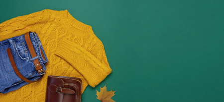 Female orange knitted sweater, blue jeans, leather bag and autumn leaves on green background top view flat lay Fashion Lady Clothes Set Trendy Cozy Knit Jumper Autumn accessories Female fashion lookの写真素材