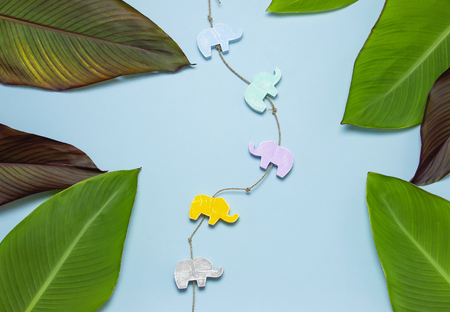 Tropical palm leaves and multi-colored childrens wooden toys in the form of elephants on blue background top view with copy space. Minimal nature summer concept Flat lay.の写真素材