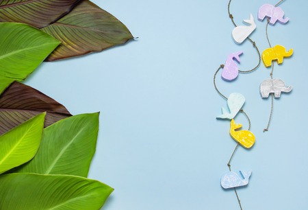 Tropical palm leaves and multi-colored childrens wooden toys in the form of elephants, whales on blue background top view with copy space. Minimal nature summer concept Flat lay.の写真素材