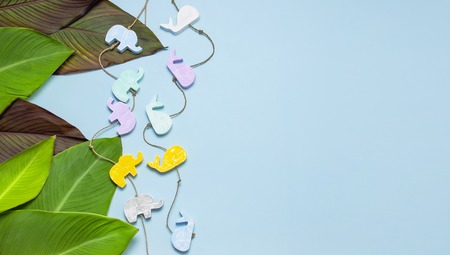 Tropical palm leaves and multi-colored childrens wooden toys in the form of elephants, whales on blue background top view with copy space. Minimal nature summer concept Flat lay.の写真素材