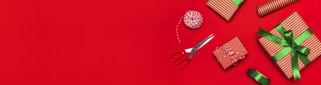 Gift boxes, packing paper, scissors, ribbon on red background. Festive background, congratulation, gift wrapping, Christmas and new year theme. Flat lay, top view copy space.の写真素材