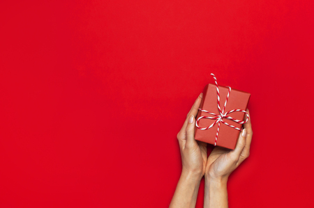 Gift box with decorative lace in female hands on red background top view flat lay. Holiday concept new year or Christmas gift box presents Xmas holiday Congratulations background with space for textの写真素材