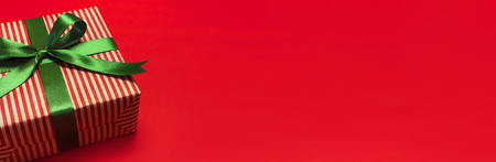 Gift box with green ribbon on red background top view flat lay. Holiday concept, birthday gift, new year or Christmas gift box presents Xmas holiday. Congratulations background with space for text.の写真素材